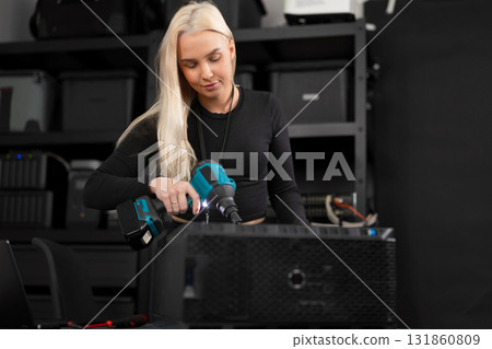 Female IT technician in a computer lab maintain and clean server hardware with a dust blower, performing maintenance 131860809