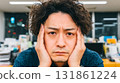 Stressed Japanese businessman sitting alone at modern office desk with hands on temples looking down 131861224