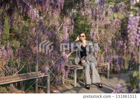 Wisteria Flowers Woman Bench - A woman sits on a bench under a wisteria trellis in a garden. Wisteria Flowers Woman Bench - A woman sits on a bench under a wisteria trellis in a garden. 131861311