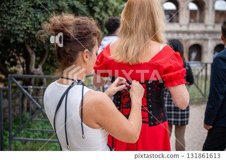 Woman helping friend tie corset on red dress near Colosseum in Rome Italy Woman helping friend tie corset on red dress near Colosseum in Rome Italy 131861613