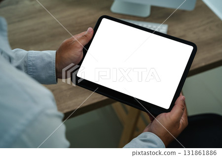 Hands holding a digital tablet with a blank white screen clean mockup for app UI, website, or presentation. Modern office desk background with ample copy space for design replaces your design mockup 131861886