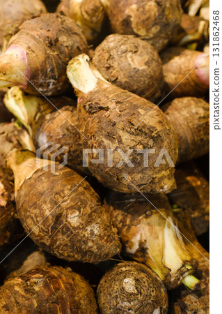 Fresh taro roots stacked together at a local market, showcasing their earthy textures and vibrant skin during a busy morning in a tropical region 131862468