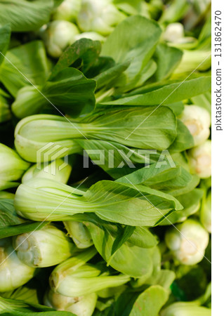 Fresh bok choy stacked in a vibrant market stall on a sunny day, ideal for healthy meals and cooking enthusiasts looking for organic vegetables 131862470