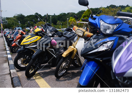 Motorcycles parked in a busy lot near a green landscape on a sunny day in a tropical location with clear skies Motorcycles parked in a busy lot near a green landscape on a sunny day in a tropical location with clear skies 131862473