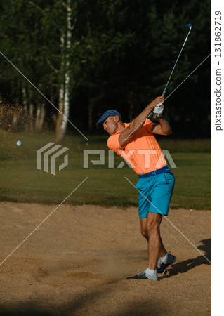 Golfer swings club in brightly colored outfit on a sunny day at a lush golf course surrounded by trees Golfer swings club in brightly colored outfit on a sunny day at a lush golf course surrounded by trees 131862719