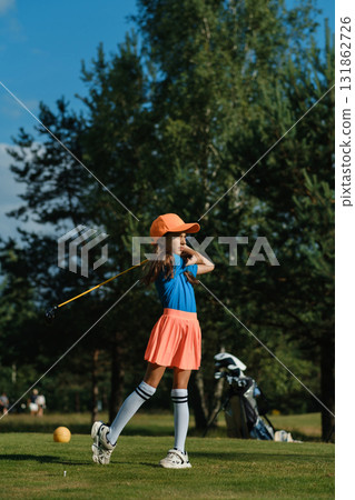 Young girl practicing golf swing on a sunny day at the green park surrounded by trees, showcasing focus and enthusiasm for the sport 131862726