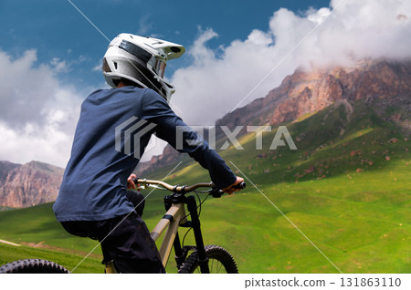 Man sits on a bicycle in a green field with mountains in the background. Concept of mountain biking and outdoor training 131863110