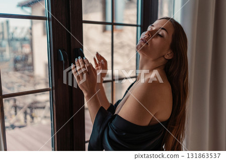 Woman window morning light illuminates serene woman standing by window with closed eyes and raised hands 131863537