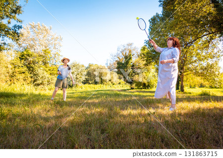 Mother and daughter having fun playing badminton on green grass in public park. Concept of family time, active lifestyle and healthy recreation. Wide shot Mother and daughter having fun playing badminton on green grass in public park. Concept of family time, active lifestyle and healthy recreation. Wide shot 131863715