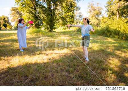 Real mother and daughter playing frisbee and enjoying family vacation in a park with trees and lawn. Outdoor connection, active lifestyle and childhood joy. Real mother and daughter playing frisbee and enjoying family vacation in a park with trees and lawn. Outdoor connection, active lifestyle and childhood joy. 131863716