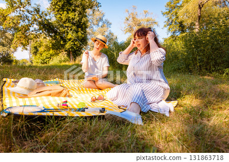 Mother and grown-up daughter enjoying afternoon rest in a park, lying on a picnic blanket. Womens conversation and wellness. Mother and grown-up daughter enjoying afternoon rest in a park, lying on a picnic blanket. Womens conversation and wellness. 131863718