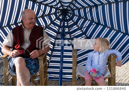 Grandfather and granddaughter relaxing together under an umbrella on a hot summer day in Portugal Grandfather and granddaughter relaxing together under an umbrella on a hot summer day in Portugal 131866840
