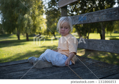 Sad blonde girl sitting alone in the park. autistic child avoiding play with other kids Sad blonde girl sitting alone in the park. autistic child avoiding play with other kids 131866853