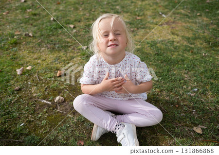 4 year old girl sitting on the grass making a painful grimace does not want to go anywhere 4 year old girl sitting on the grass making a painful grimace does not want to go anywhere 131866868