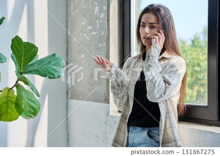 Serious teenage female standing at home talking on smartphone 131867275