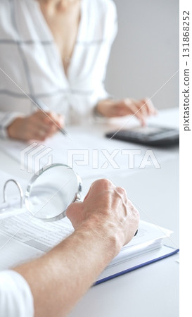 Close up of accountant hand using a magnifying glass and a calculators, to audit financial reports in brightly lit office. Audit and taxes concept Close up of accountant hand using a magnifying glass and a calculators, to audit financial reports in brightly lit office. Audit and taxes concept 131868252
