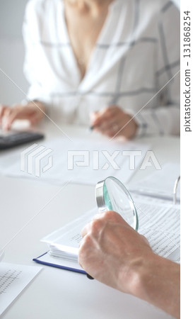Groupe of professional accountants working together, using a magnifying glass and a calculators, to audit financial reports in their brightly lit office. Audit and taxes concept 131868254