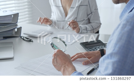 Accounting professionals analyzing financial documents, checking spreadsheet details with calculator and magnifying glass. Audit and taxes in business Accounting professionals analyzing financial documents, checking spreadsheet details with calculator and magnifying glass. Audit and taxes in business 131868297