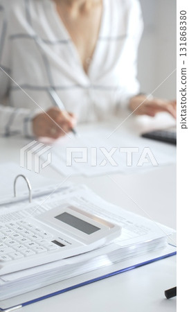 Close up of a calculator on financial documents, with an accountant taking notes, emphasizing accounting, finance, and tax preparation. Audit and taxes in business Close up of a calculator on financial documents, with an accountant taking notes, emphasizing accounting, finance, and tax preparation. Audit and taxes in business 131868380