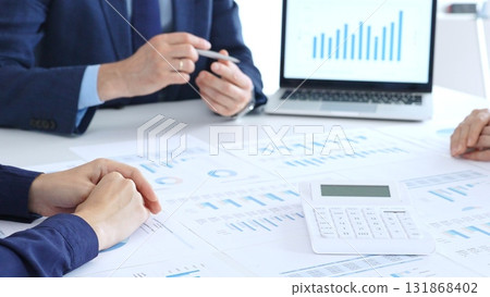 Business people collaborating at a conference table, reviewing financial charts and reports, using a laptop and calculator while engaging in discussions about strategy and performance. Accouters at Business people collaborating at a conference table, reviewing financial charts and reports, using a laptop and calculator while engaging in discussions about strategy and performance. Accouters at 131868402