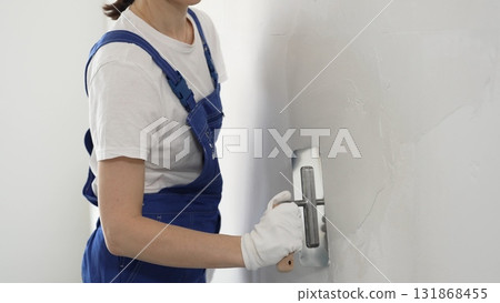 Professional female construction worker is using a finishing trowel to carefully apply plaster on a wall, demonstrating expertise in home renovation and interior finishing 131868455