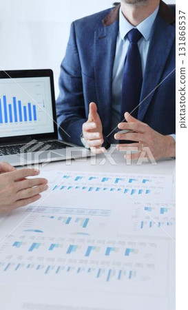 Businesspeople sitting at the table and pointing into financial charts while discussing financial data, market trends during meeting in modern office. Business people concept 131868537