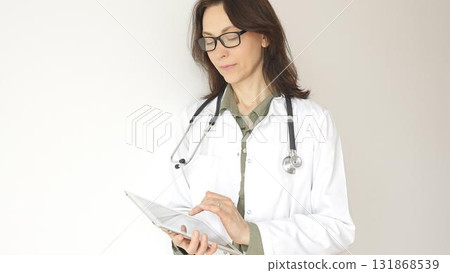 Portrait of a female physician reviewing patient records on digital tablet, standing in contemporary medical workspace with natural lighting. Medicine and health care concept 131868539