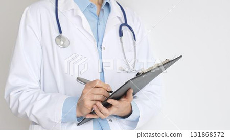 Close up of female doctor wearing stethoscope and white coat over blue blouse is standing and writing on a black clipboard, representing medical expertise and patient care. Medicine and health care 131868572