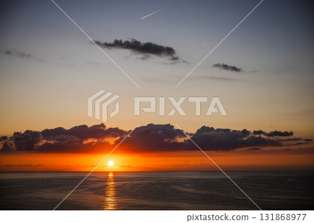 Sunrise over the Mediterranean Sea with golden light reflecting on the calm water and dark clouds hovering above the horizon in Spain. Sunrise over the Mediterranean Sea with golden light reflecting on the calm water and dark clouds hovering above the horizon in Spain. 131868977