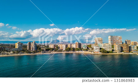 Aerial drone view of Alicante city coast in Spain with tall modern buildings, sandy beach, and calm Mediterranean sea on a bright summer day Aerial drone view of Alicante city coast in Spain with tall modern buildings, sandy beach, and calm Mediterranean sea on a bright summer day 131868983