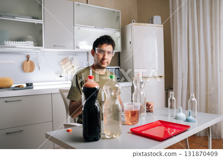 Agricultural technician wearing safety glasses preparing fertilizer in home kitchen laboratory, mixing various liquids and using syringe for diy gardening approach. Concept of urban farming. Agricultural technician wearing safety glasses preparing fertilizer in home kitchen laboratory, mixing various liquids and using syringe for diy gardening approach. Concept of urban farming. 131870409