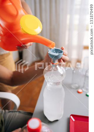 Closeup cropped shot of unrecognizable gardeners mixing fertilizer, filling bottle with water through funnel from watering can, showcasing sustainable agricultural method for plant growth. 131870499
