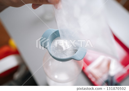 Extreme close-up of unrecognizable man pouring organic fertilizer through funnel into plastic bottle, mixing nutrient-rich solution for healthy garden plants. Concept of home gardening. 131870502
