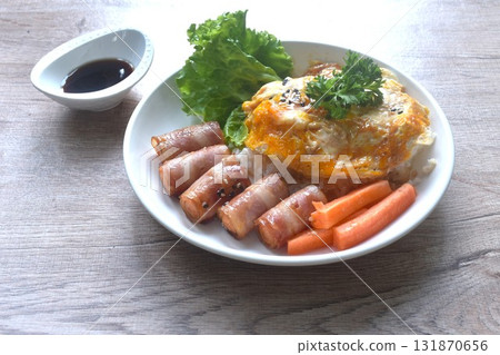 fried creamy egg omelet topping plain rice with pork bacon roll sausage and carrot dipping Japanese teriyaki sauce on plate  131870656