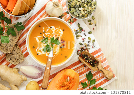 Pumpkin soup puree from the ingredients of a pumpkin, carrot, potato, ginger, onion, garlic, spices on a white wooden background. Autumn cream soup. 131870811
