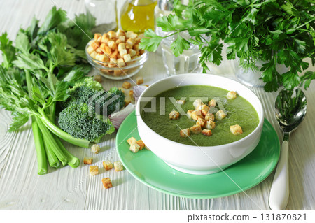 Healthy soup puree of broccoli, celery and herbs with croutons in white bowl ready to eat next to ingredients on a white wooden background. Close-up. Healthy soup puree of broccoli, celery and herbs with croutons in white bowl ready to eat next to ingredients on a white wooden background. Close-up. 131870821