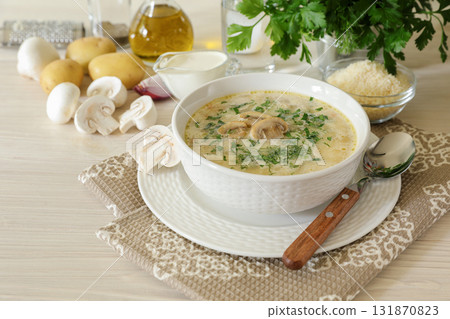 Tasty champignon mushrooms soup with cream and cheese in white bowl on white wooden background 131870823