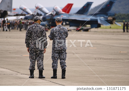 Two soldiers in front of a row of parked fighter jets 131871175