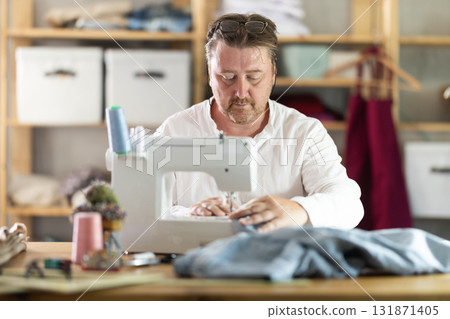 Man seamstress operating by sewing machine, manufactures clothing 131871405