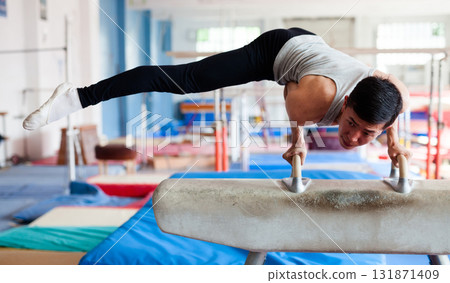 Male athlete doing complicated exciting trick on pommel horse in professional gym 131871409