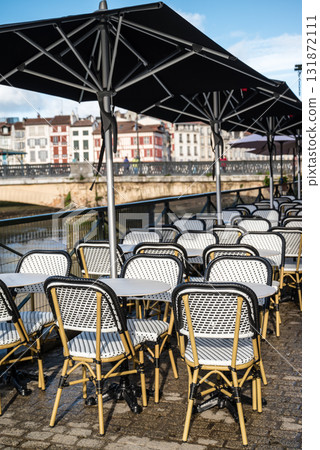 Tables lined up in front of riverside restaurants and a streetscape of historic buildings in Bayonne, Basque Country, France 131872111