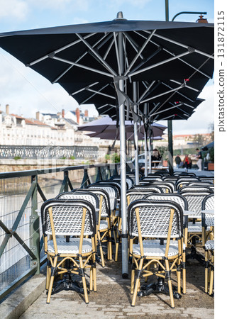 法國巴斯克地區巴約訥河畔餐廳前排列整齊的餐桌和歷史建築的街景 131872115