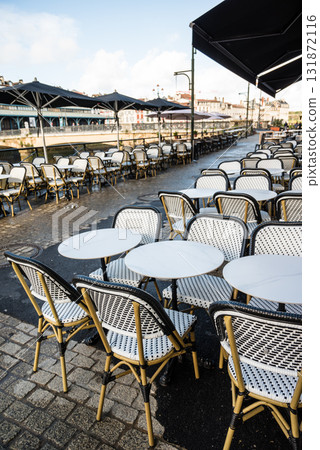 法國巴斯克地區巴約訥河畔餐廳前排列整齊的餐桌和歷史建築的街景 131872116