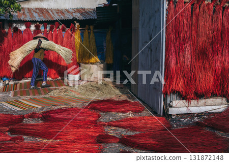 Vietnamese woman in a traditional straw hat dries dyed reeds for production of woven mats at factory in an artisan village in Vietnam 131872148