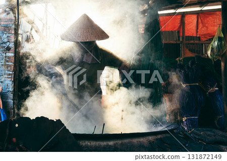 Vietnamese woman worker in straw hat dyes reeds in boiling water on stove at a woven mat factory in Vietnam Vietnamese woman worker in straw hat dyes reeds in boiling water on stove at a woven mat factory in Vietnam 131872149