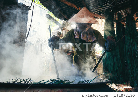 Vietnamese woman worker in straw hat dyes reeds in boiling water on stove at a woven mat factory in Vietnam Vietnamese woman worker in straw hat dyes reeds in boiling water on stove at a woven mat factory in Vietnam 131872150