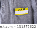 Guest badge with yellow border is clipped to pocket of gray shirt, indicating visitor status. badge stands out against fabric, suggesting formal or organized event 131872622