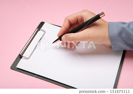 Woman holding pen and black clipboard with paper on pink background. Woman holding pen and black clipboard with paper on pink background. 131873111
