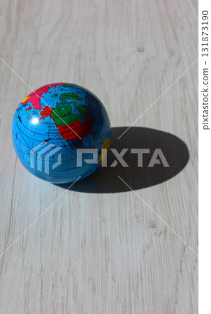 A vertical photo of a globe with the American continents visible in the light and its shadow cast on a wooden plank. An illustrative photo for the theme of light and time zones on different continents 131873190