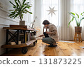 Young woman crouching to clean bookshelf near floor, holding books during detailed home cleaning 131873225